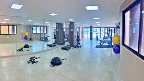 Un gimnasio con equipamiento de ejercicio, espejos y un ventanal grande.
