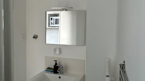 Une salle de bain avec un lavabo blanc, un miroir, un four à micro-ondes et une grille de ventilation.