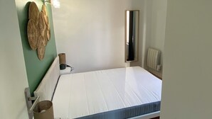 Une petite chambre à coucher, bien rangée, avec un lit simple, une table de chevet, un miroir et un radiateur.