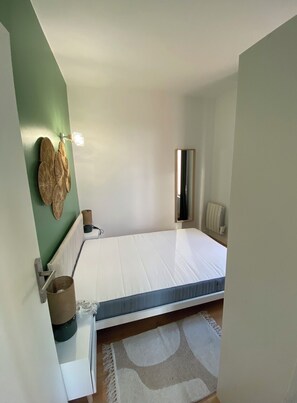Ein kleines, ordentlich eingerichtetes Schlafzimmer mit einem Einzelbett, einem Nachttisch, einem Spiegel und einer Heizung.