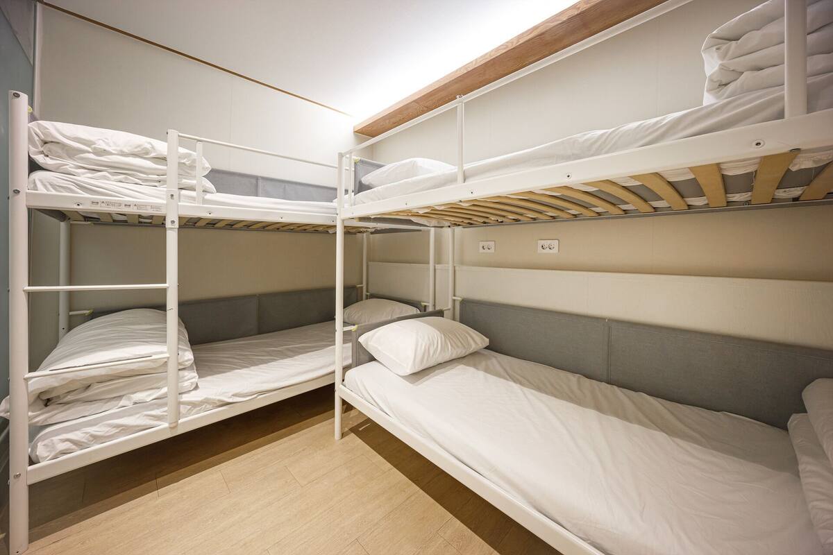 Quarto com beliche, teto de madeira e chão em tons claros.