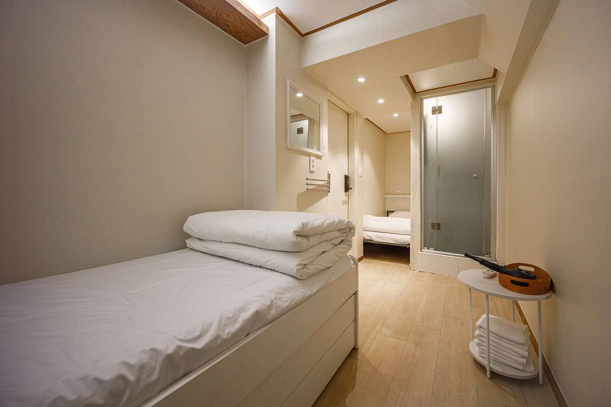 Quarto com cama, mesa de cabeceira com abajur, espelho e porta que dá para outro cômodo.