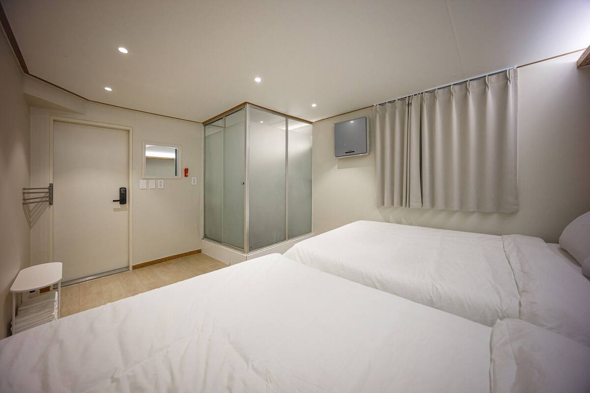 Quarto de hotel com duas camas, chuveiro, espelho, televisão e cortina.