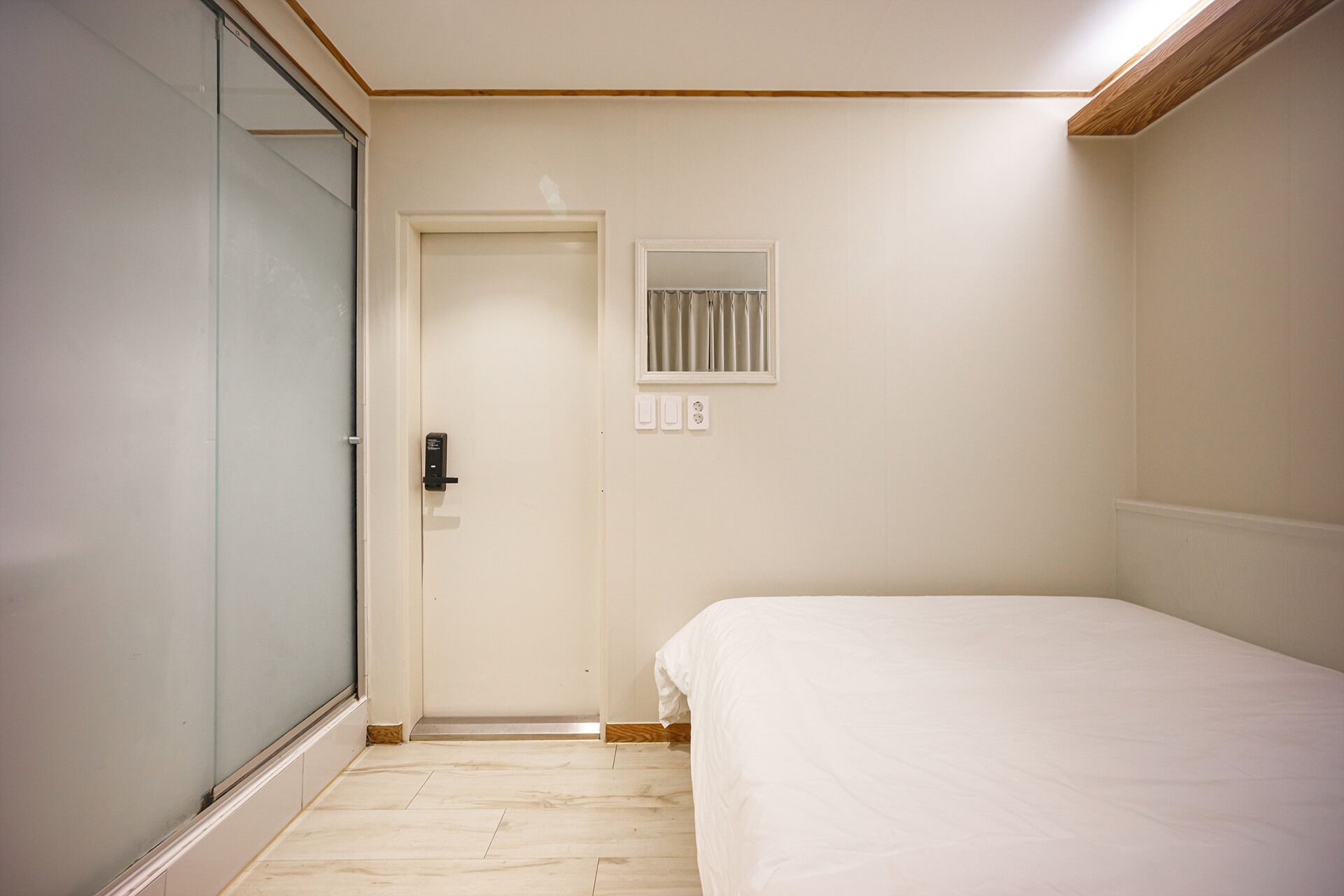 A bedroom with a bed, a door, a small window, and a light switch.