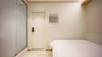 A bedroom with a bed, a door, a small window, and a light switch.