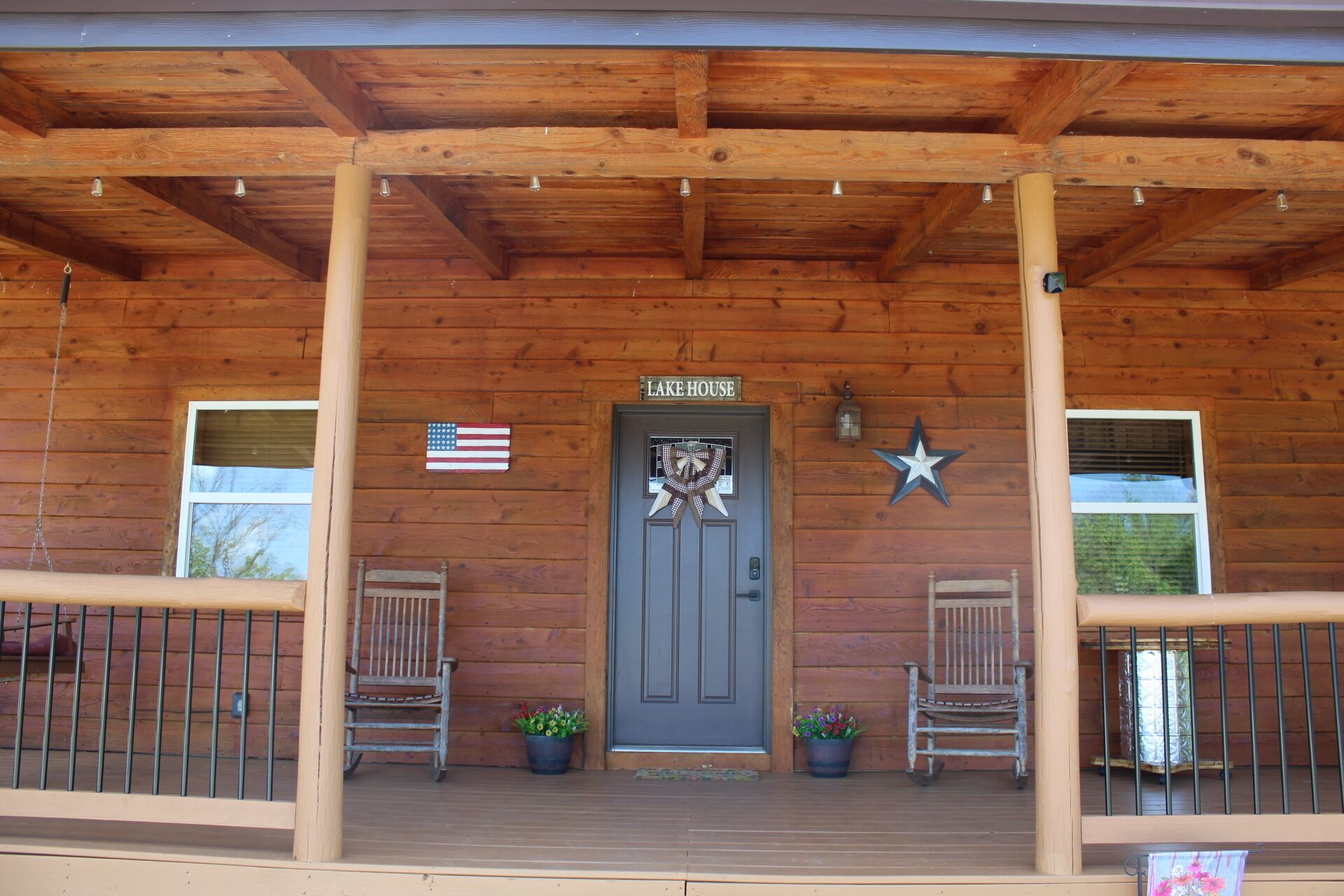 A wooden cabin with a porch, two rocking chairs, a door with a star decoration, and an American flag.