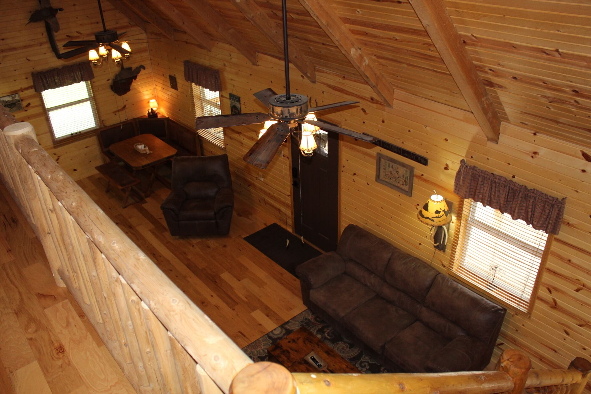 A wooden cabin interior with a ceiling fan, a sofa, a chair, and a dining table.
