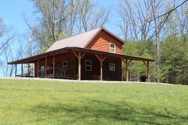 A wooden cabin with a porch, a picnic table, and a grill area.