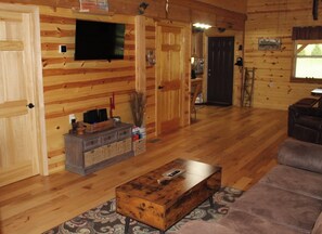 A wooden interior with a television, a sofa, a coffee table, and a fireplace.