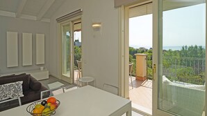 A modern living room with a dining table, a sofa, a fruit bowl, and a balcony with a view. - Montecolo Resort E7 by Wonderful Italy (Manerba del Garda)