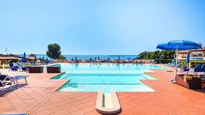 A swimming pool with blue lounge chairs and umbrellas, surrounded by a tiled deck. - Montecolo Resort E7 by Wonderful Italy (Manerba del Garda)
