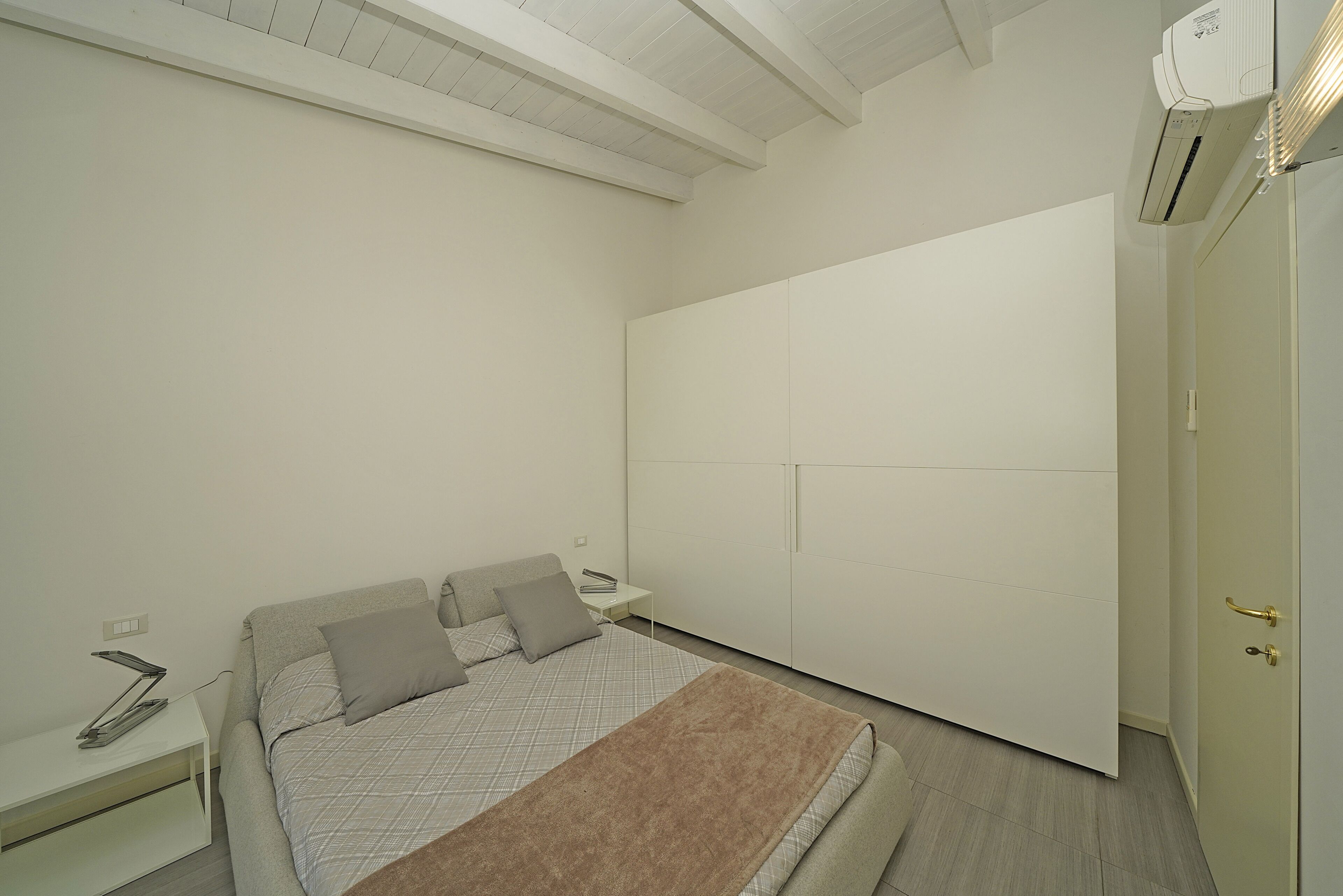 A bedroom with a bed, bedside tables, a wardrobe, and an air conditioning unit.