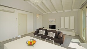 A modern living room with a sofa, TV, and a fruit bowl on a table. - Montecolo Resort E7 by Wonderful Italy (Manerba del Garda)