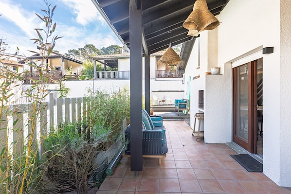 A covered patio with outdoor furniture, a white fence, and a view of neighboring buildings.