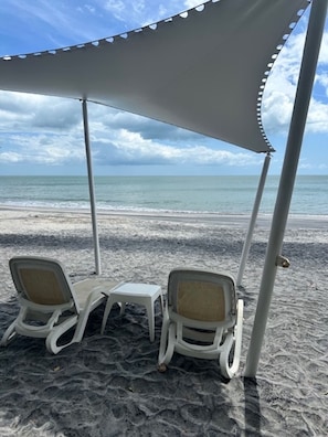 A beach with two white lounge chairs and a small table under a white canopy.