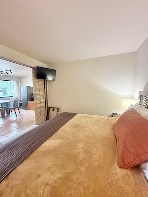 A hotel room with a bed, a TV mounted on the wall, a desk with a chair, and a view of the outside.