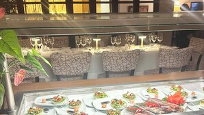 A restaurant with a glass display case filled with various dishes, a plant, and a seating area with patterned chairs and tables. - Coronado Luxury Club & Suites - 1 bedroom- Green fees for 2 & resort access (Panamá Oeste Province)