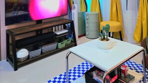 A living room with a flat-screen TV, a wooden entertainment unit, a table with a checkered table runner, and yellow curtains. - Dyad Suites Pasay (Pasay)