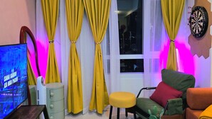 A living room with a television, a cactus on a table, a dartboard, and yellow curtains. - Dyad Suites Pasay (Pasay)