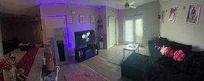 A living room with a TV, a sofa, a coffee table, a fireplace, and a door leading to another room.