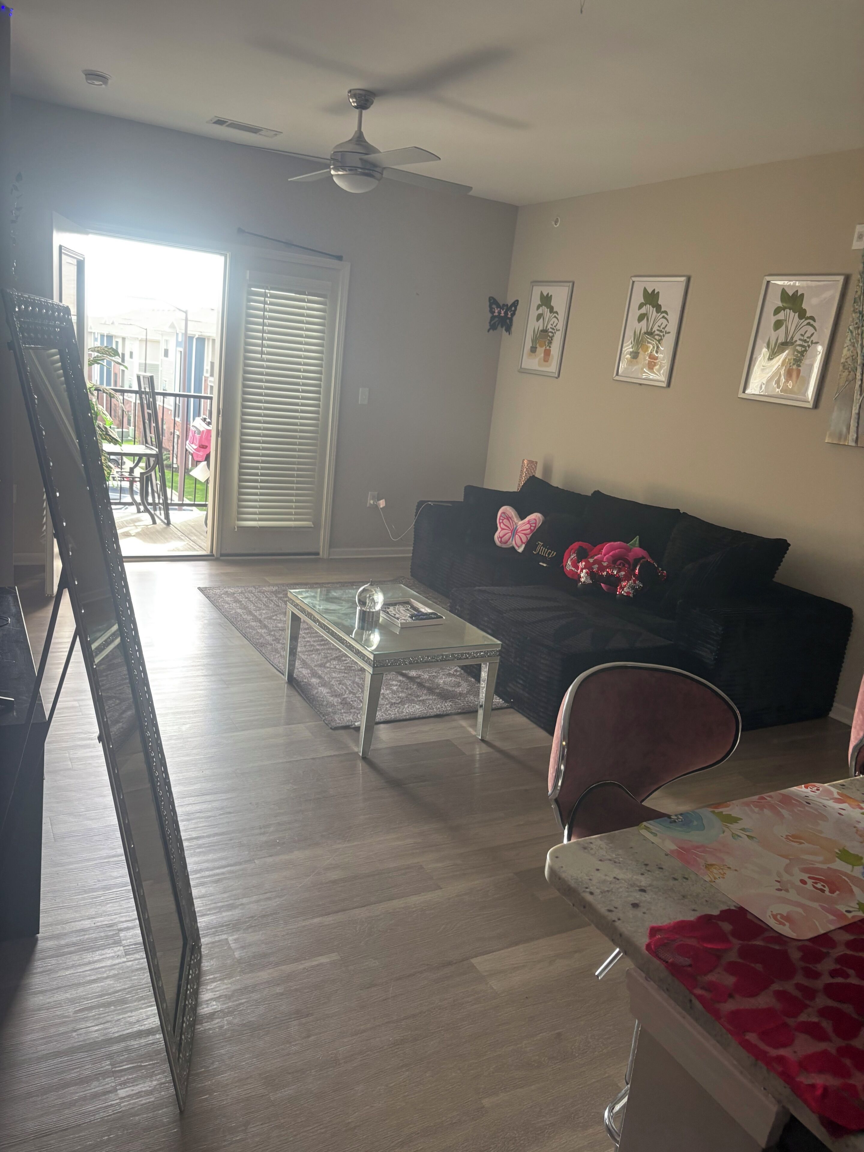 Una sala de estar con un sofá, una mesa de centro, una silla, un ventilador de techo y un puerta corrediza de vidrio que da a un espacio exterior.