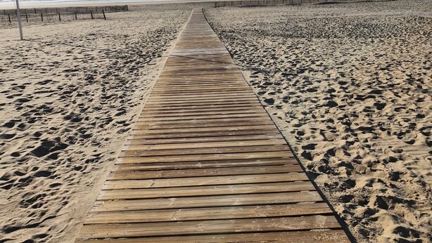 Een houten looppad dat naar een strand leidt, met een heldere lucht en de oceaan op de achtergrond.