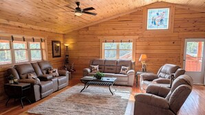 A log cabin interior with a high ceiling, wooden walls, a ceiling fan, a fireplace, and a large window. - NEW Klondike Cabin, Saguache CO (Saguache)