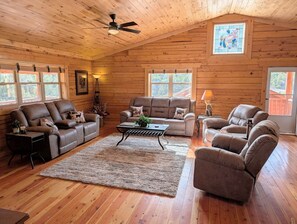 A log cabin interior with a high ceiling, wooden walls, a ceiling fan, a fireplace, and a large window. - NEW Klondike Cabin, Saguache CO (Saguache)