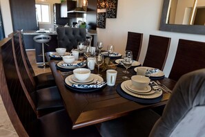 Una mesa de comedor dispuesta con platos, tazones y vasos, rodeada de sillas de madera oscura.