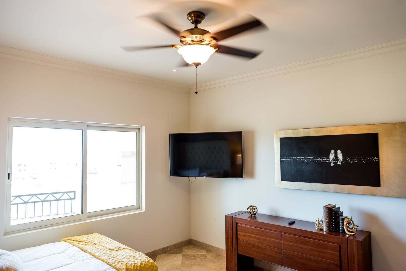 A bedroom with a bed, a ceiling fan, a TV, a painting, and a dresser.