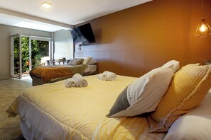 Ein Hotelzimmer mit Bett, einem an der Wand montierten Fernseher und einem Balkon mit Tisch und Stühlen.