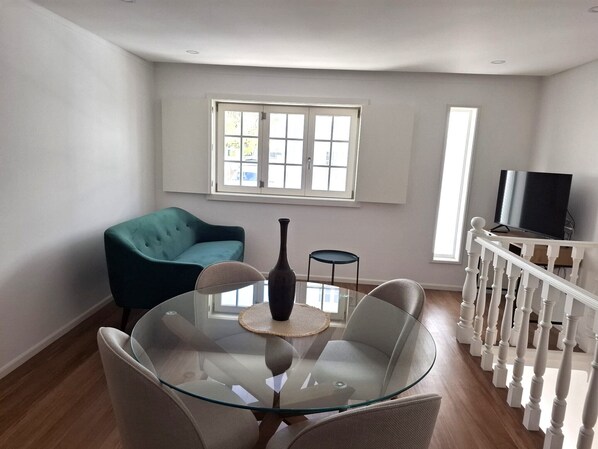 En moderne stue med et glasbord, to stole, en blå sofa, et fjernsyn og en trappe.