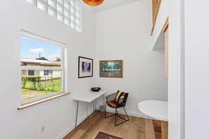 Ein Zimmer mit großem Fenster, einem weißen Tisch, einem Stuhl und einem kleinen weißen Beistelltisch.