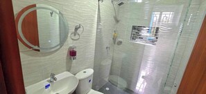 Un baño con un espejo redondo, un lavabo, un inodoro y una zona de ducha con mampara de vidrio.