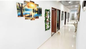 Un pasillo con varias pinturas en la pared, una puerta con espejo y una escalera que conduce a otra zona.