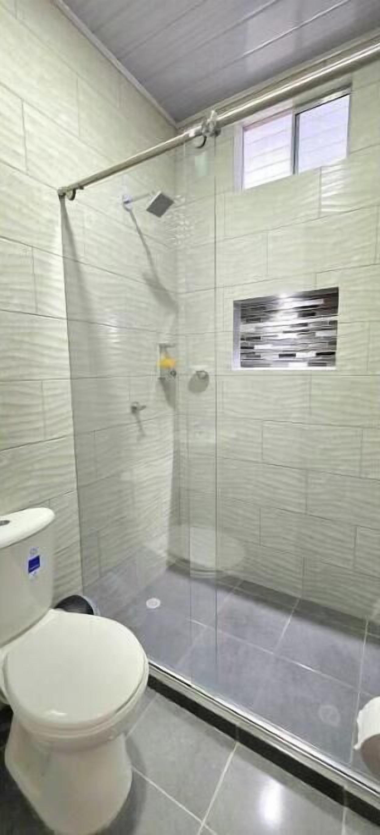 A shower with a glass door, a toilet, and a small window.