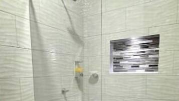 A shower with a glass door, a toilet, and a small window.