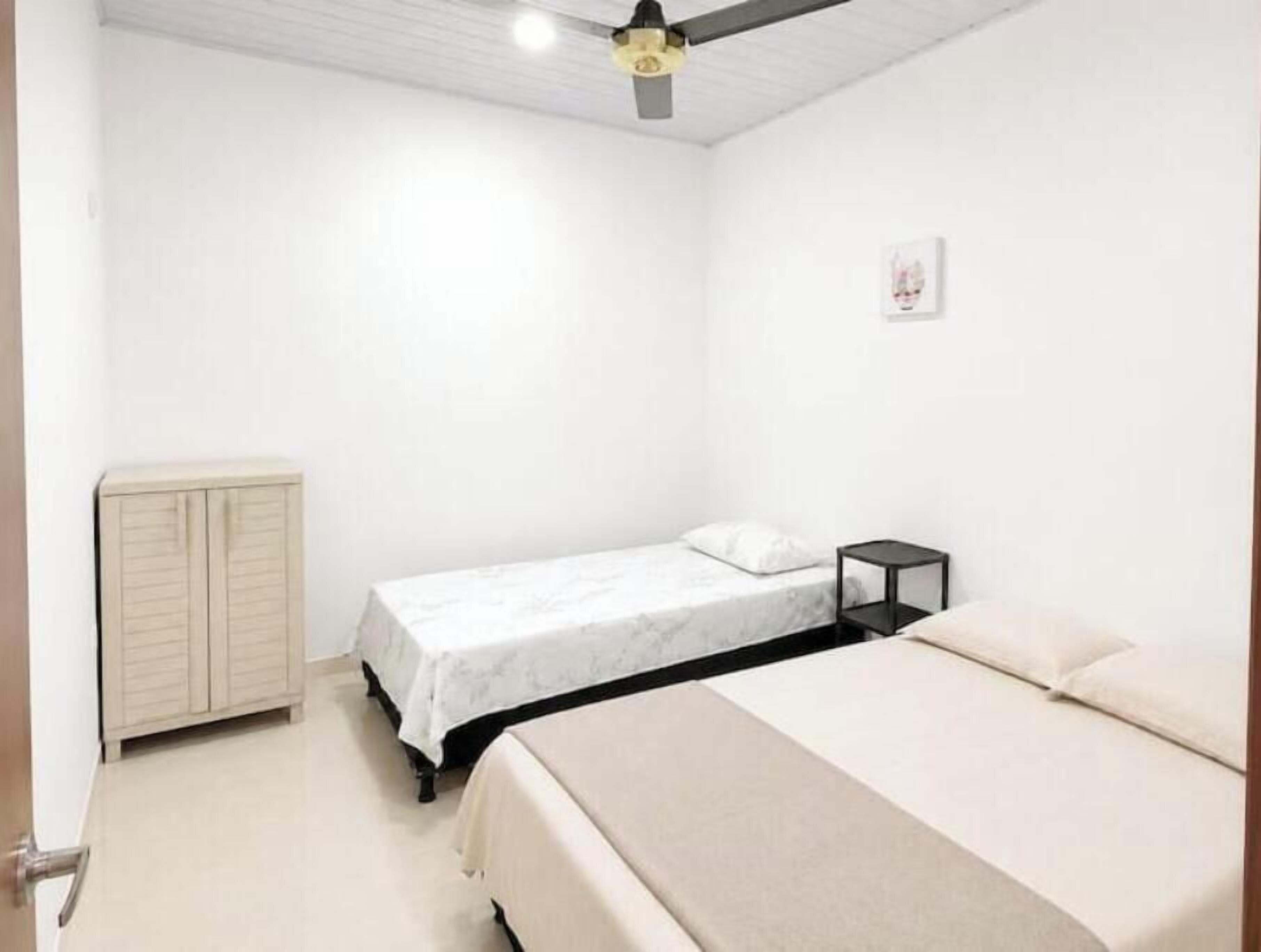 Un dormitorio con cama, mesita de noche, armario y ventilador de techo.