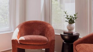 Ein Zimmer mit einem großen Fenster, einem Sessel, einem kleinen Tisch mit einer Pflanze und einem weiteren Sessel.