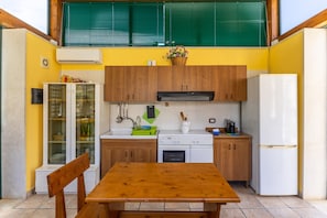 A compact kitchen with wooden cabinets, a white refrigerator, and a dining table with benches. - Country House 'Alla Corte Di Nonna Maria' with Air Conditioning (Modica)