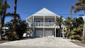 Een tweelaags huis met een balkon, een garage en palmbomen op de achtergrond.