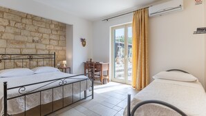 Un dormitorio con dos camas, una pared de piedra, un escritorio y vistas a través de un ventanal.