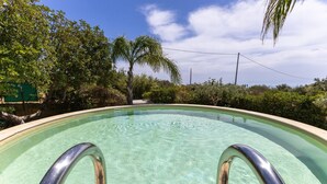 Una piscina limpia con barandales de metal, rodeada de follaje y árboles.