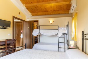 Une chambre avec des lits superposés, un bureau, une chaise, un téléviseur et un luminaire fixé au mur.