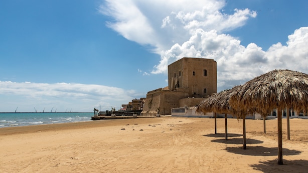 Ein sandiger Strand mit einem historischen Gebäude und einem Gebäude mit einem Reetdach.