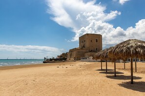 A sandy beach with a historical building and a thatched-roof structure.