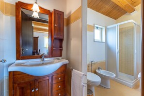 Une salle de bain avec un meuble-lavabo en bois, un lavabo, un miroir, des toilettes, un bidet et une douche.