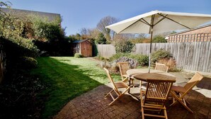 Een terras met een tafel en stoelen, een houten schutting en een tuinhuis in een achtertuin.