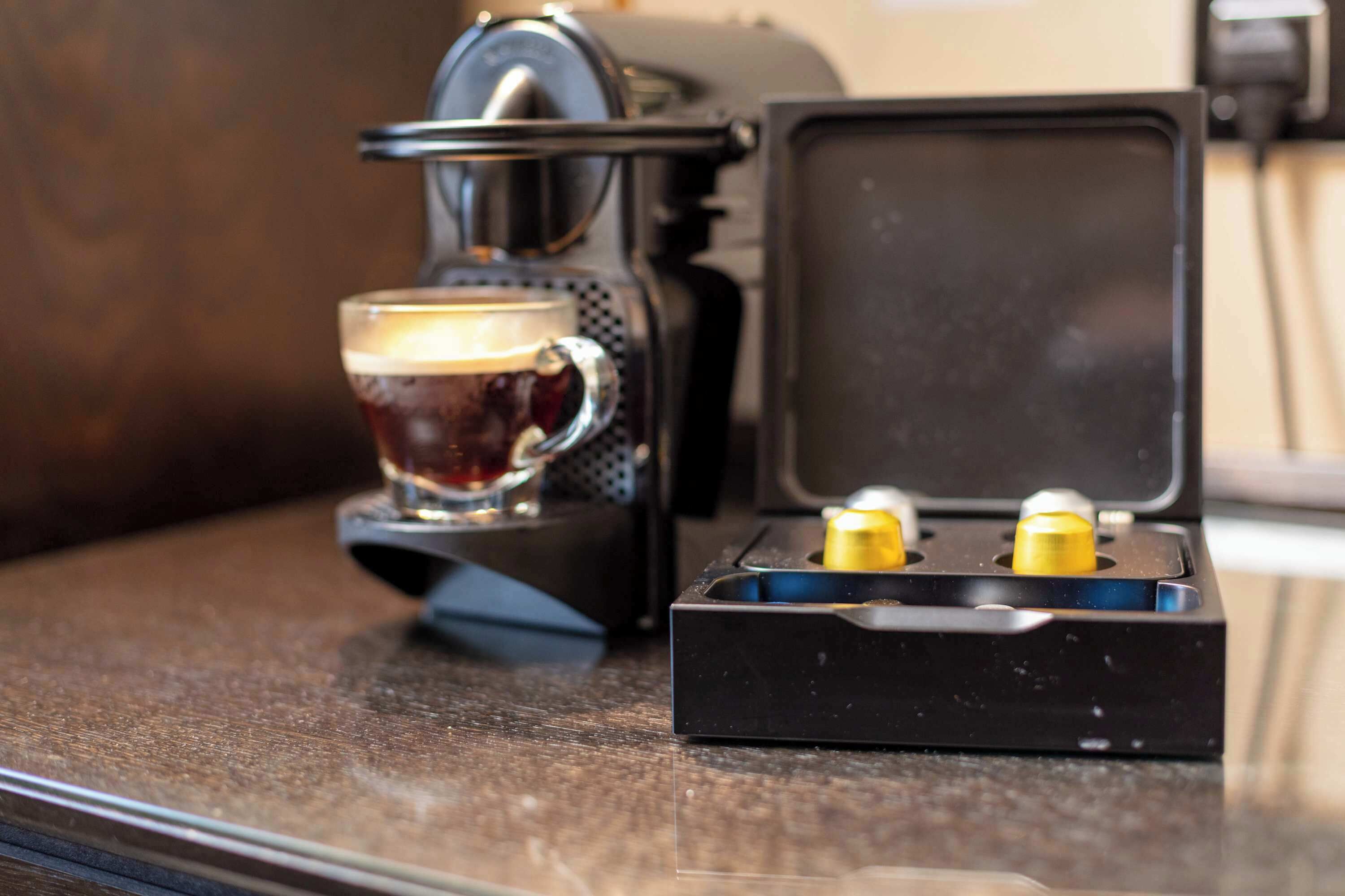Une machine à café avec une tasse de café, une prise de courant et un boîtier noir contenant des éléments jaunes et bleus.