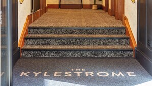 A carpeted staircase with 'The Kylestrome' written on it, leading to a room with a wooden door and a small table with a plant. - The Kylestrome Deluxe - King or Twin (Ayr)